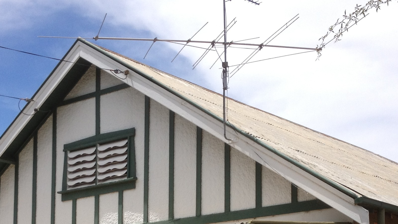 An Australian semi-detached brick dwelling with a green painted porch and gable in daylight