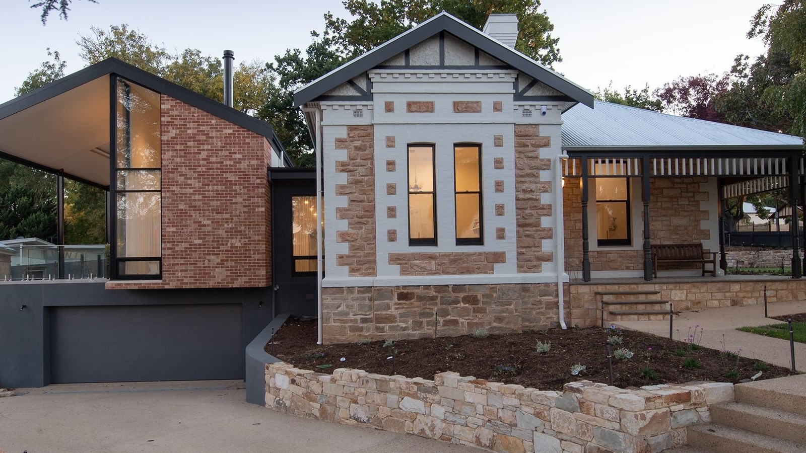 A brick veneer house exterior with rendered trim, dark roof and lit windows seen in late afternoon light