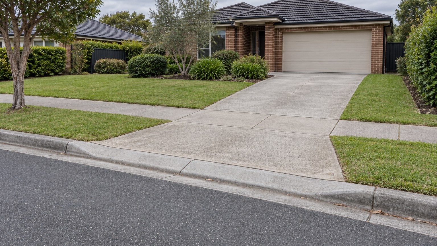 Concrete driveway crossing a suburban footpath toward a brick house